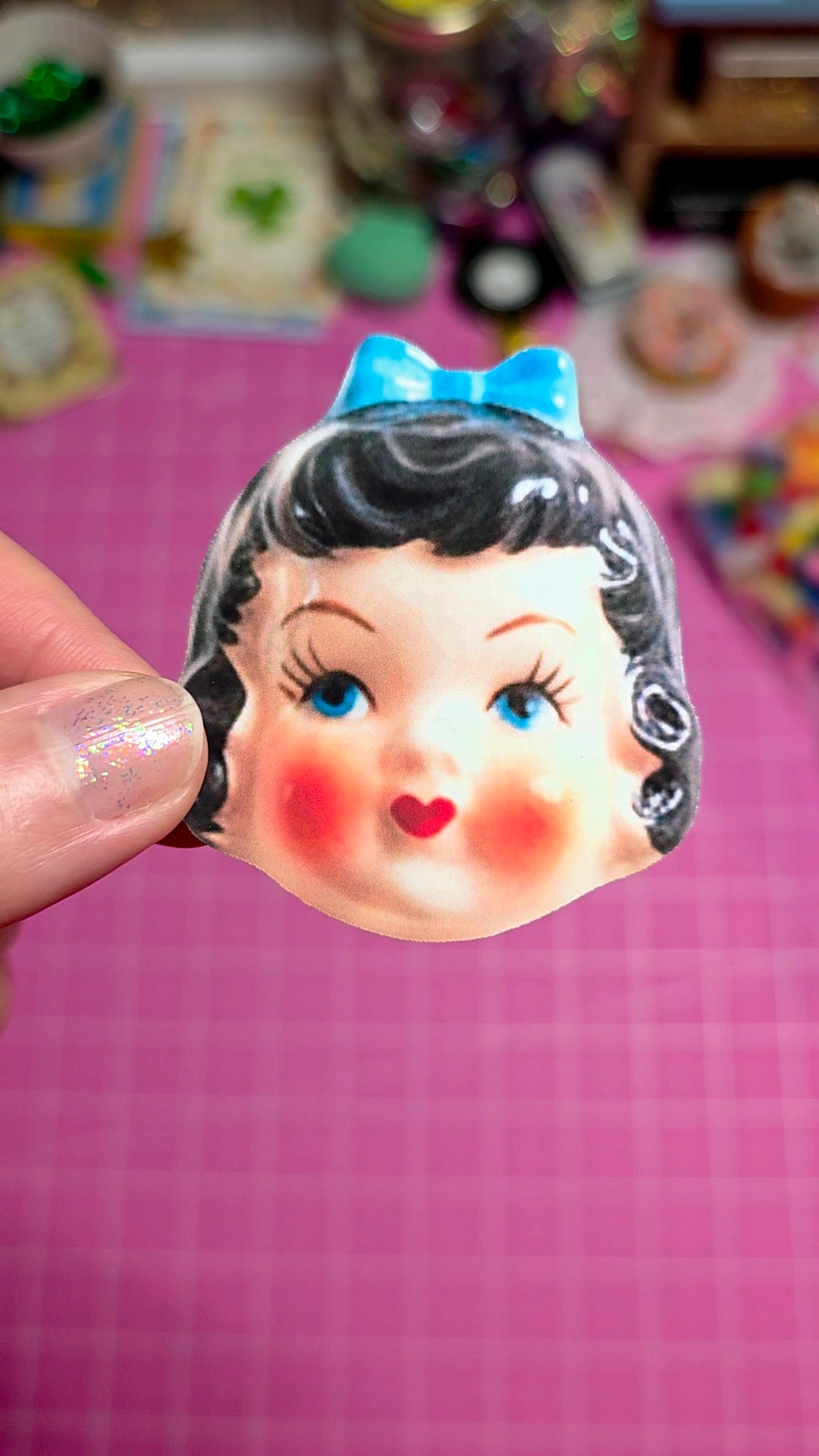 Vintage-style girl's face mask with a blue bow held over a pink checkered background.