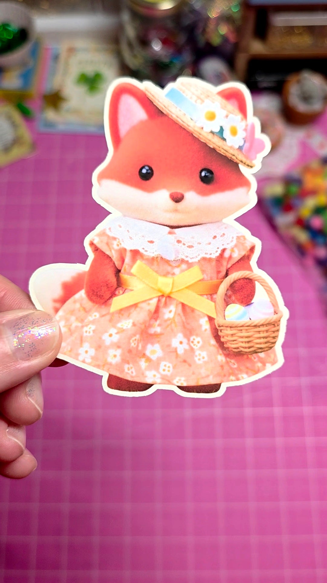 Cartoon fox character in a dress holding a basket, held against a colorful background.