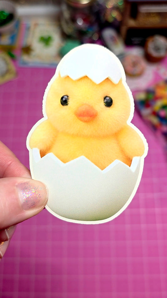 Sticker of a chick in an eggshell held by a hand on a pink background