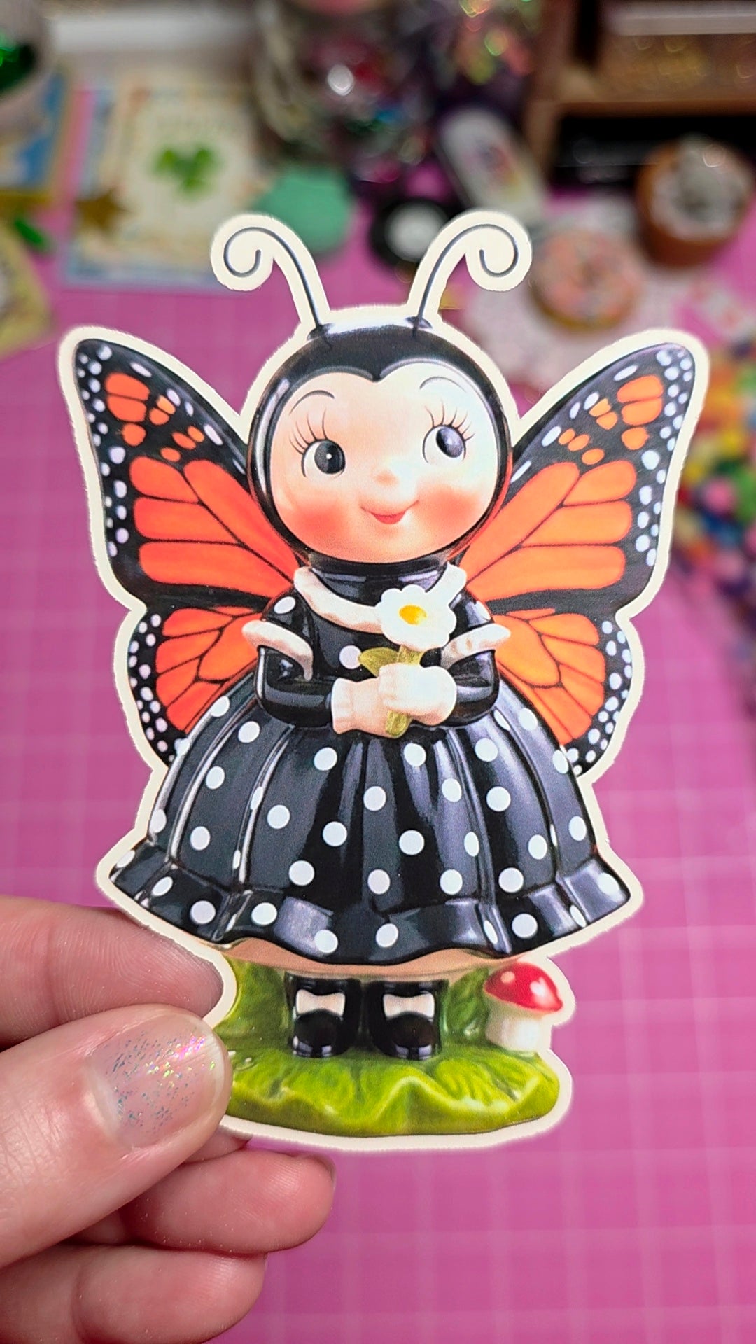 Sticker of a character with butterfly wings held against a pink background