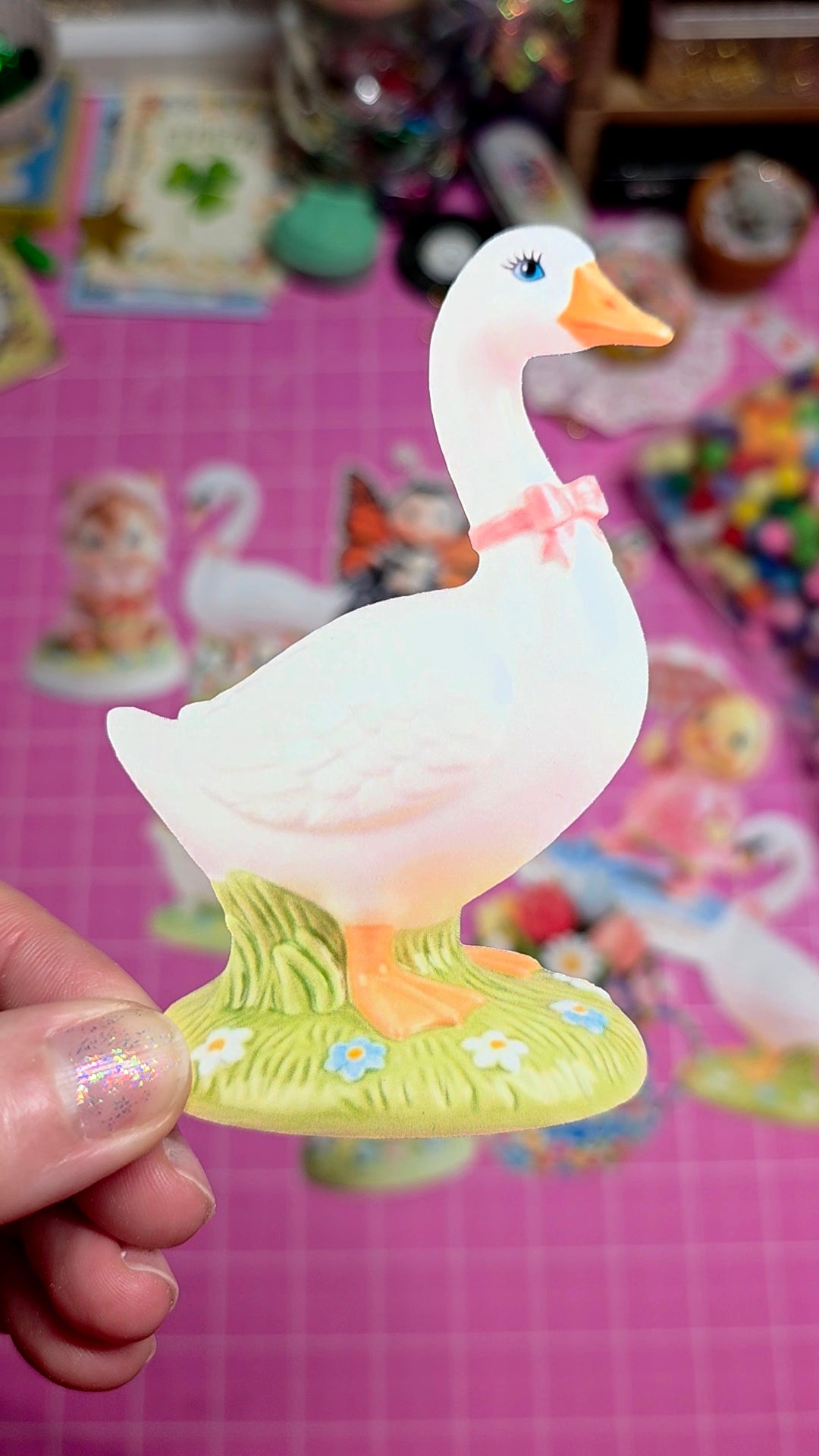 White goose figurine with a pink bow held against a colorful, blurred background