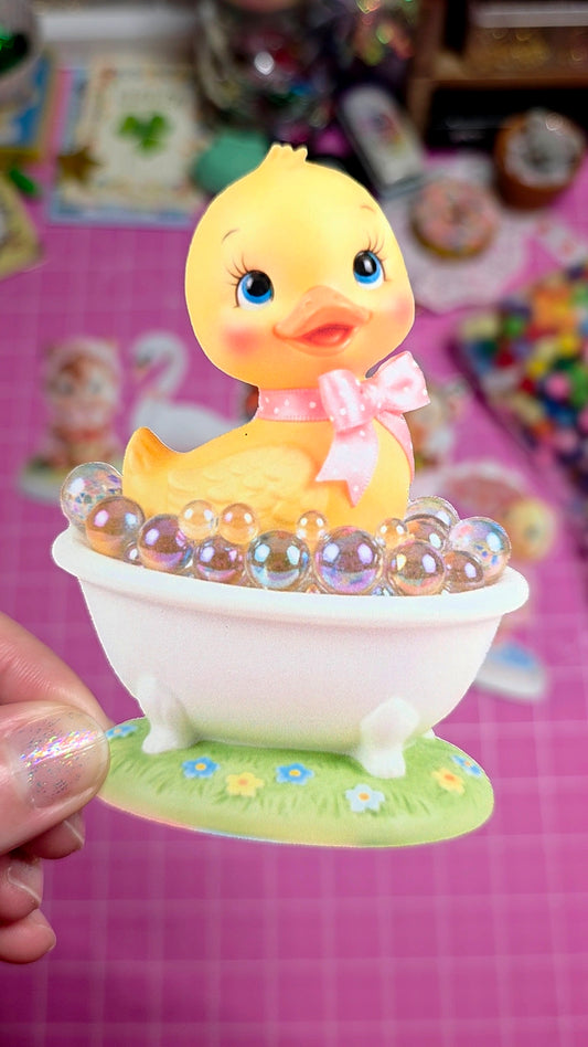 Small yellow duck figurine with a pink bow in a white bowl on a pink background