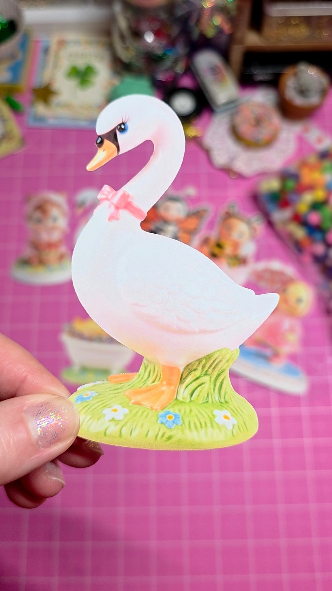 Colorful swan figurine held by a hand on a pink surface with toys in the background