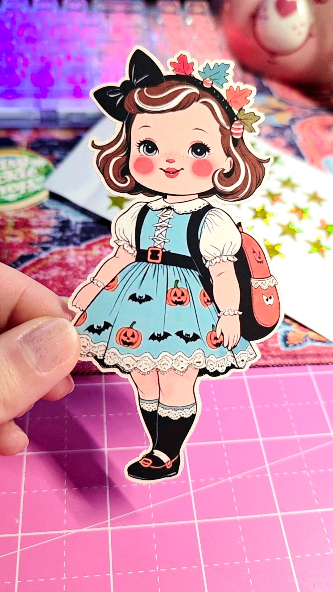 Sticker of a girl in a Halloween dress held over a pink cutting mat.
