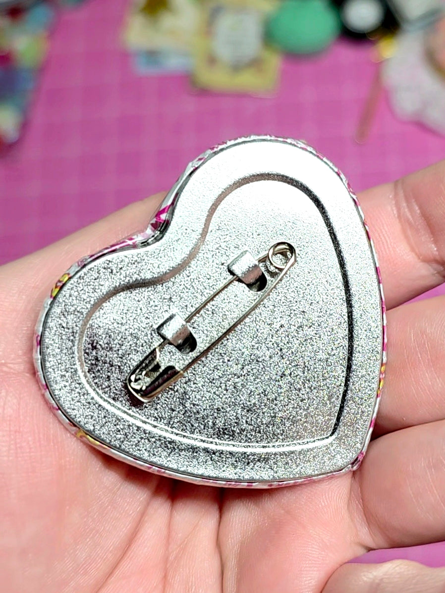 Heart-shaped silver brooch held in a hand with a colorful background