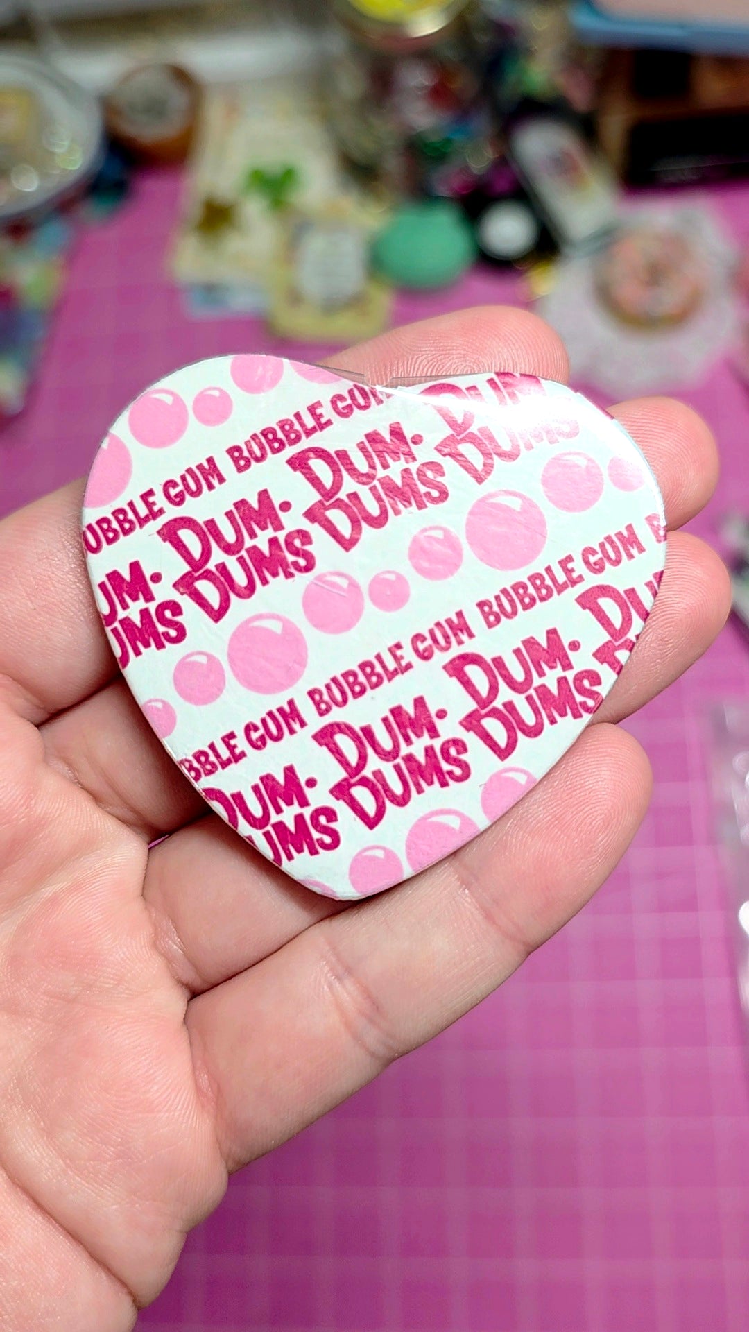 Hand holding a Dum-Dum's bubble gum shaped card with a pink and white design.