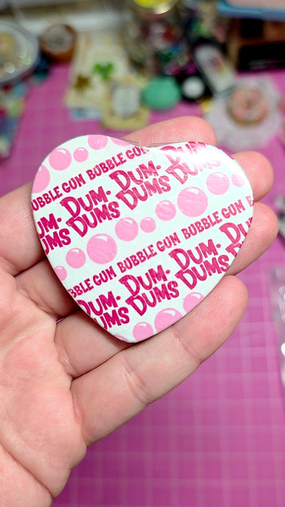 Hand holding a Dum-Dum's bubble gum shaped card with a pink and white design.