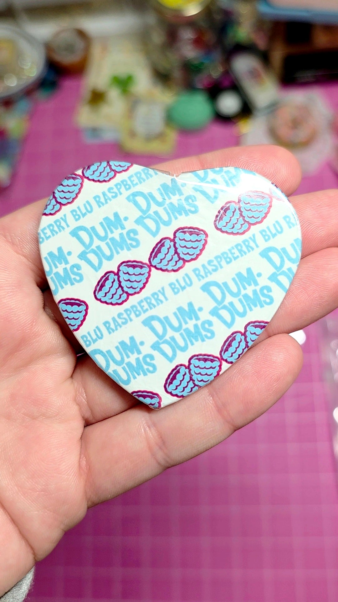 Heart-shaped Dum-Dum candy wrapper held in a hand with a blurred background