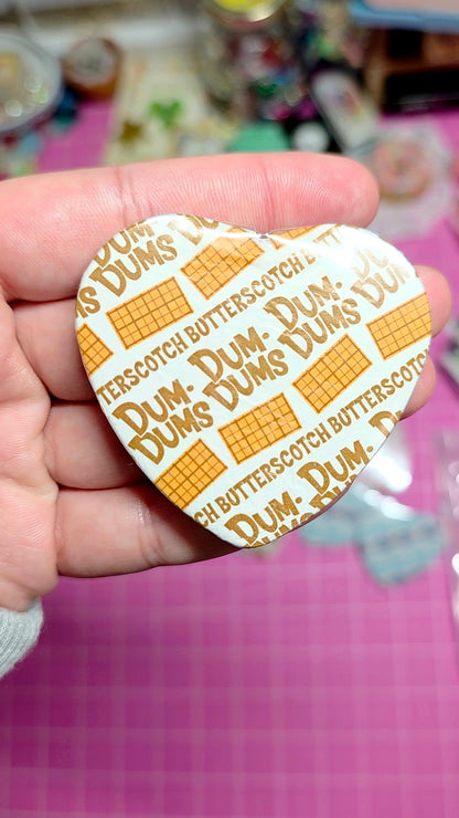 Heart-shaped Dum Dum Lollipop wrapper held by a hand with a pink background