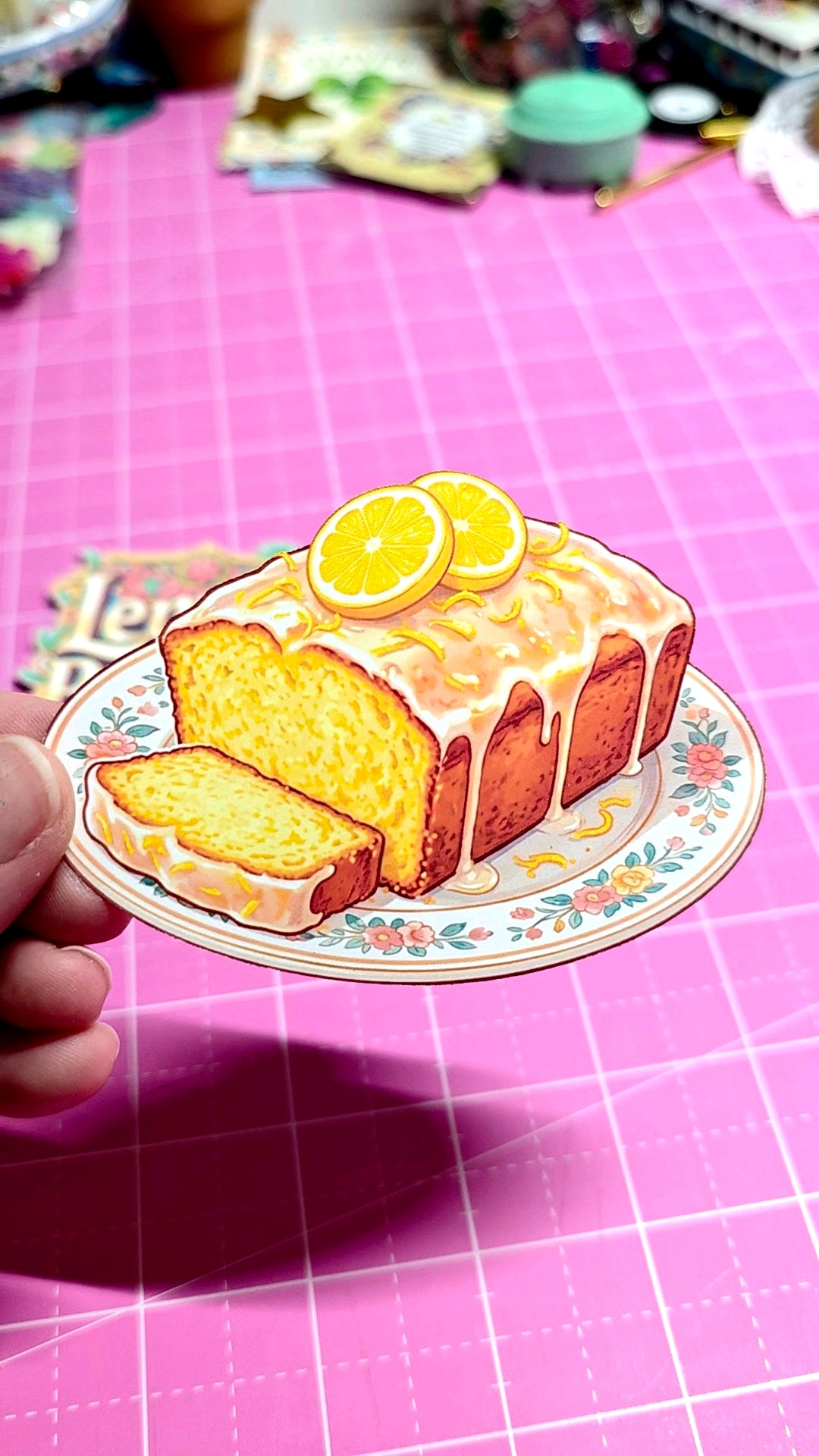 Sticker of a lemon cake with slices on a decorative plate held over a pink grid background.
