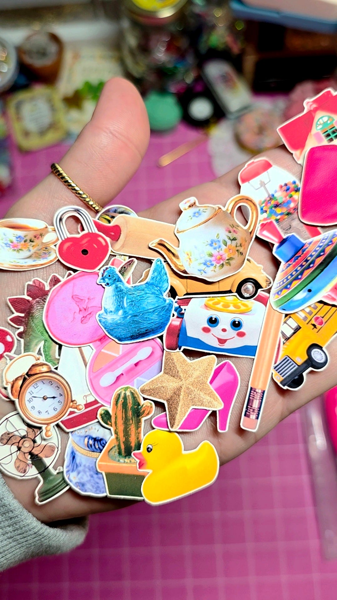 Hand holding a collection of colorful stickers with various designs on a pink surface.