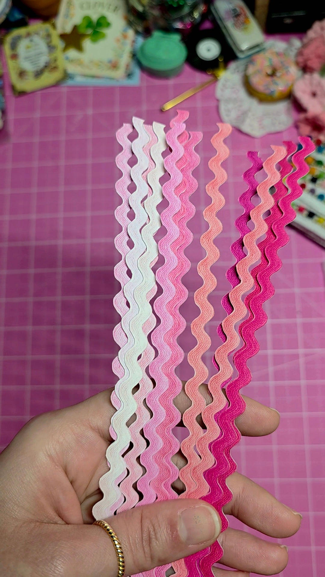 Decorative paper strips with wavy edge held by a hand on a pink checkered background
