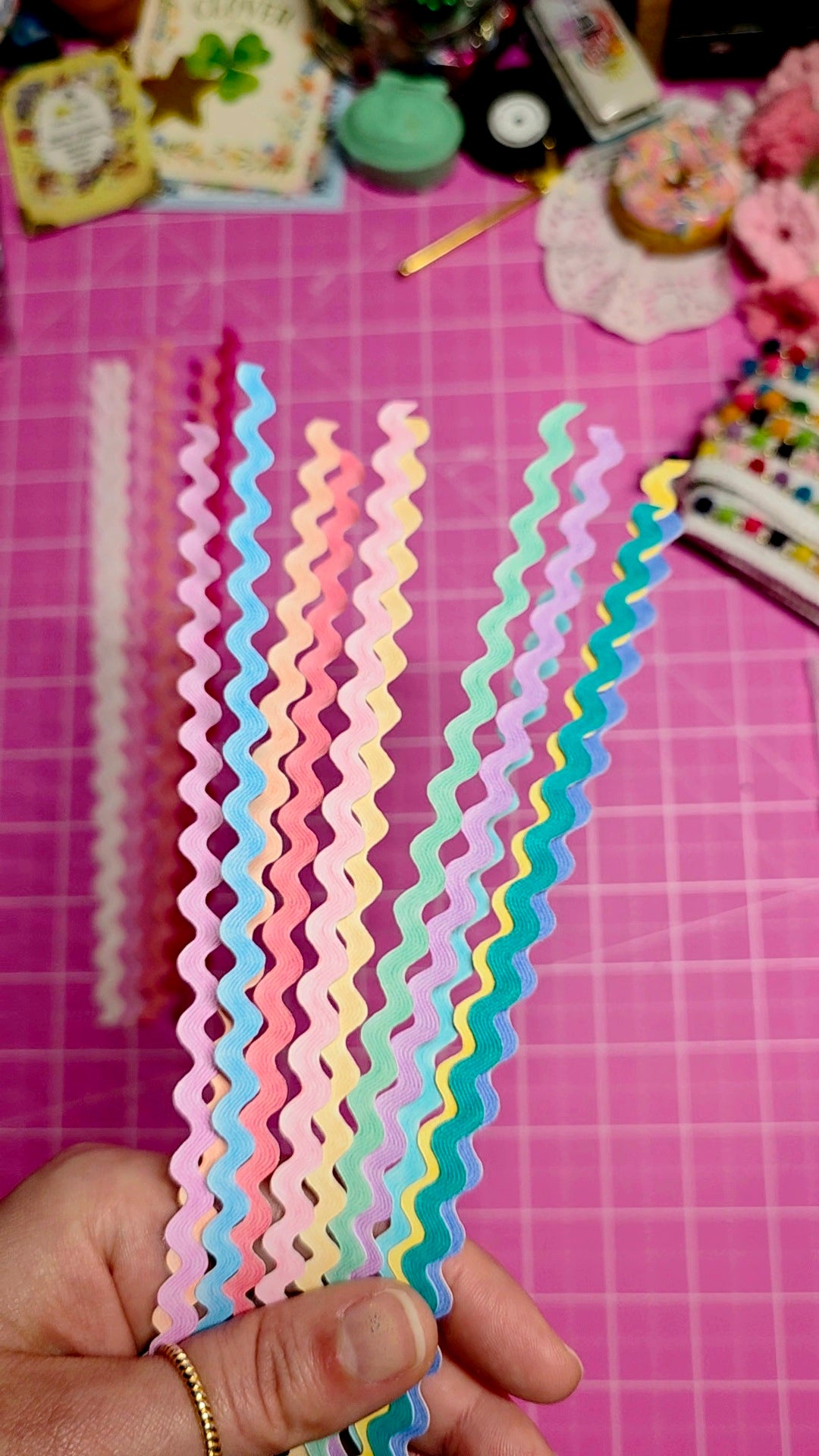 Colorful wavy paper strips held by a hand on a pink cutting mat.