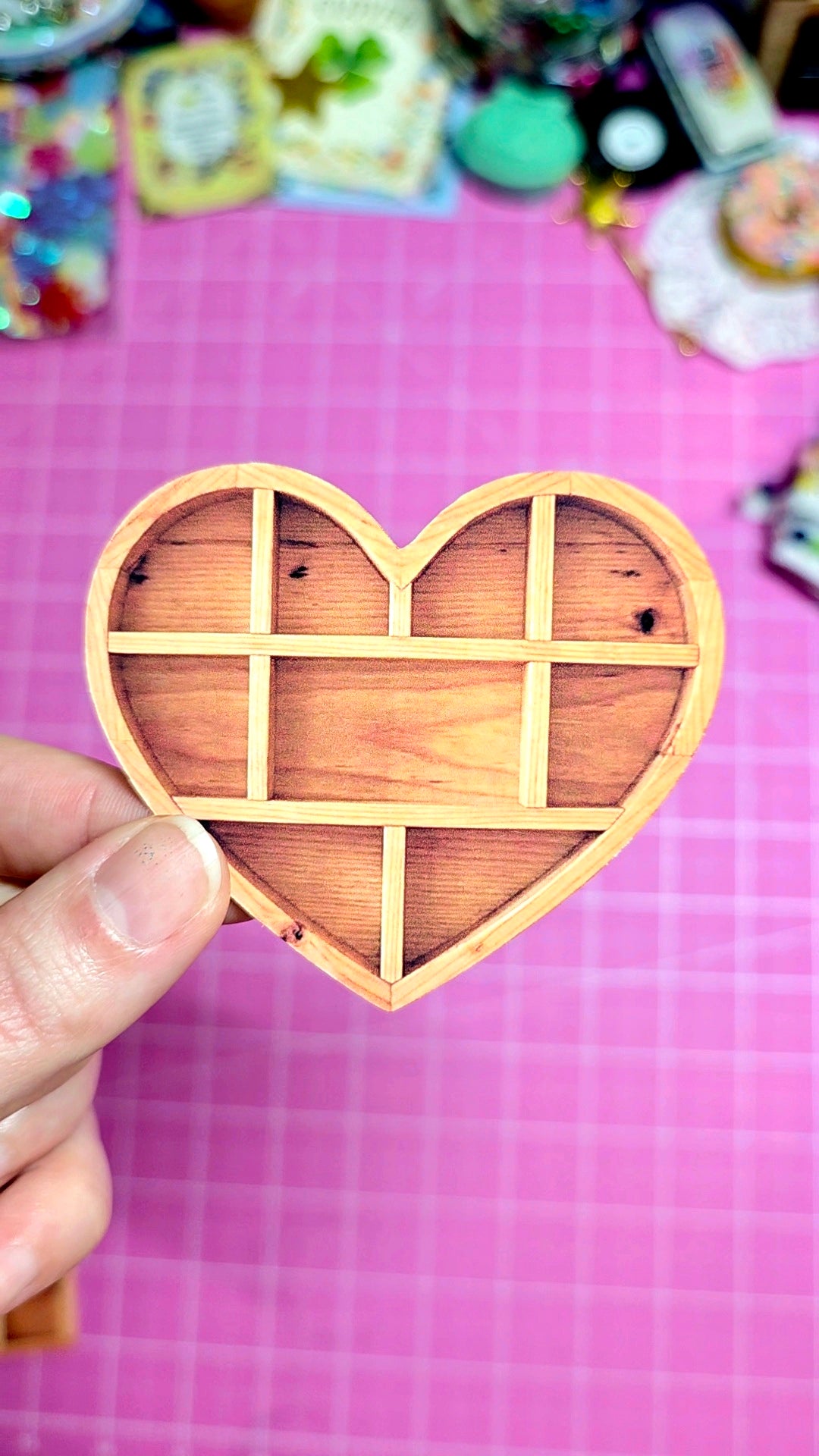 Wooden heart-shaped puzzle piece held by a hand on a pink grid background