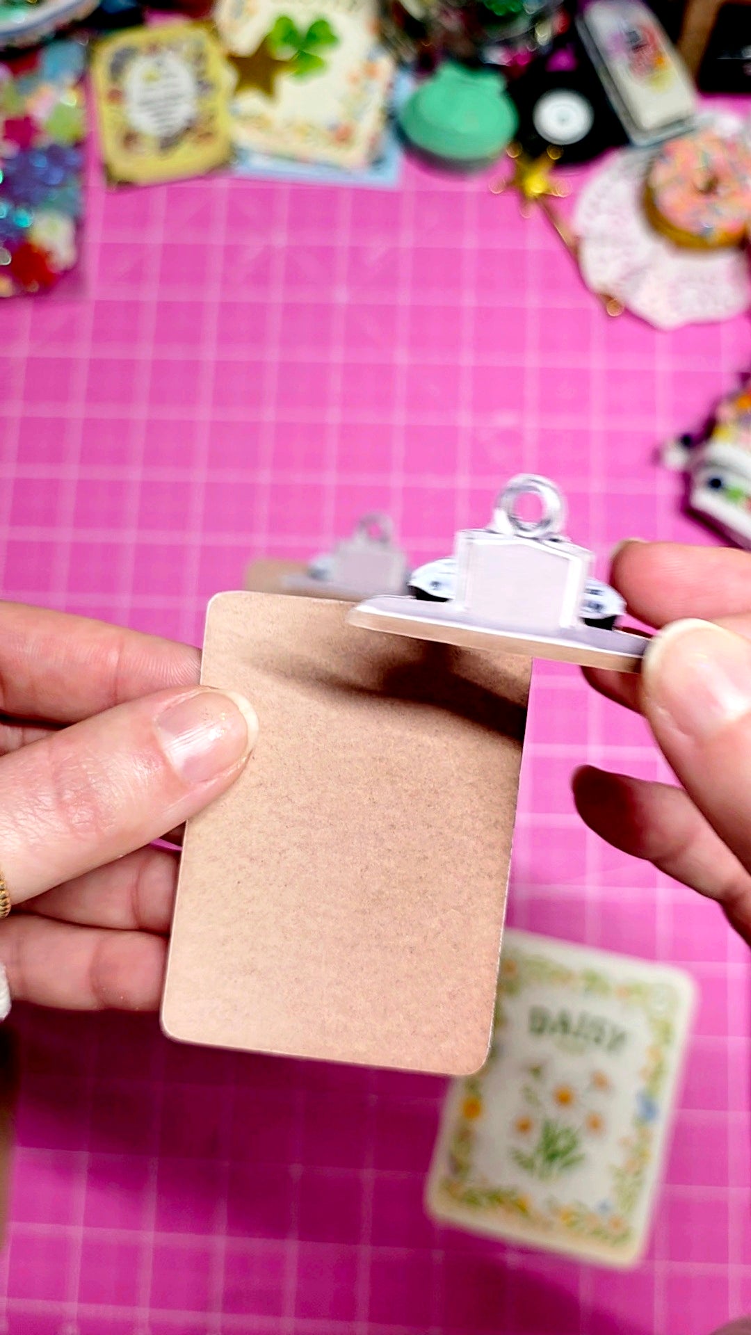 Hand holding a small card with a decorative design on a pink grid background