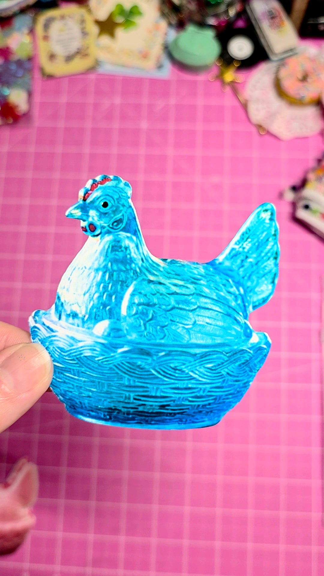 Blue glass chicken figurine on a pink grid background