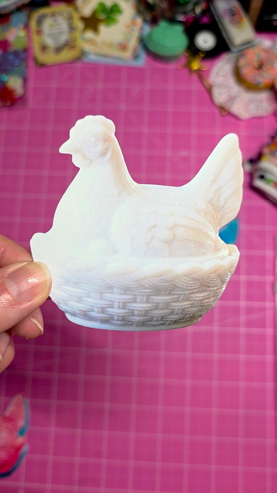 3D-printed chicken-shaped object held by a hand on a pink grid background