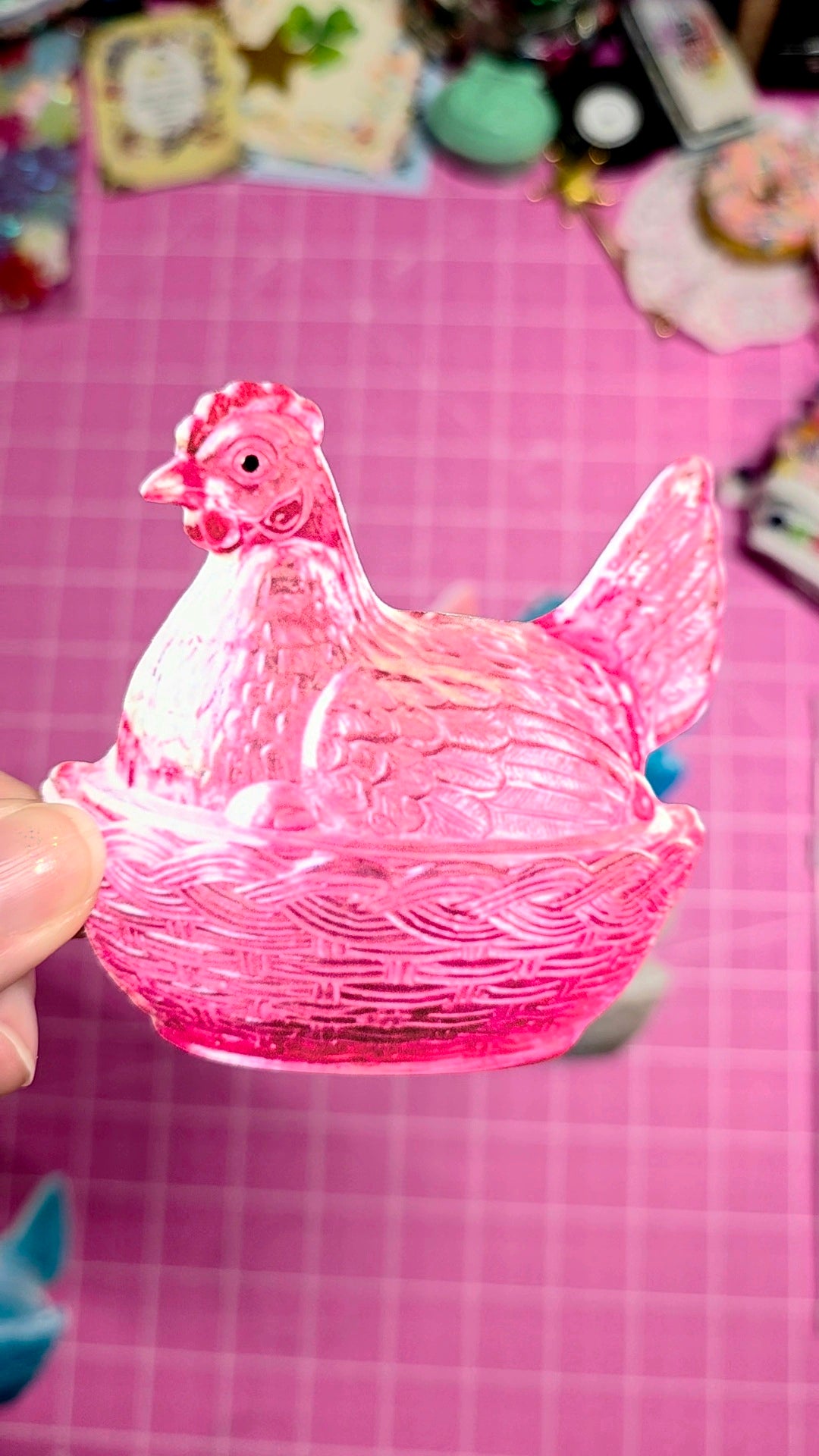 Pink glass chicken-shaped container held by a hand on a pink checkered background