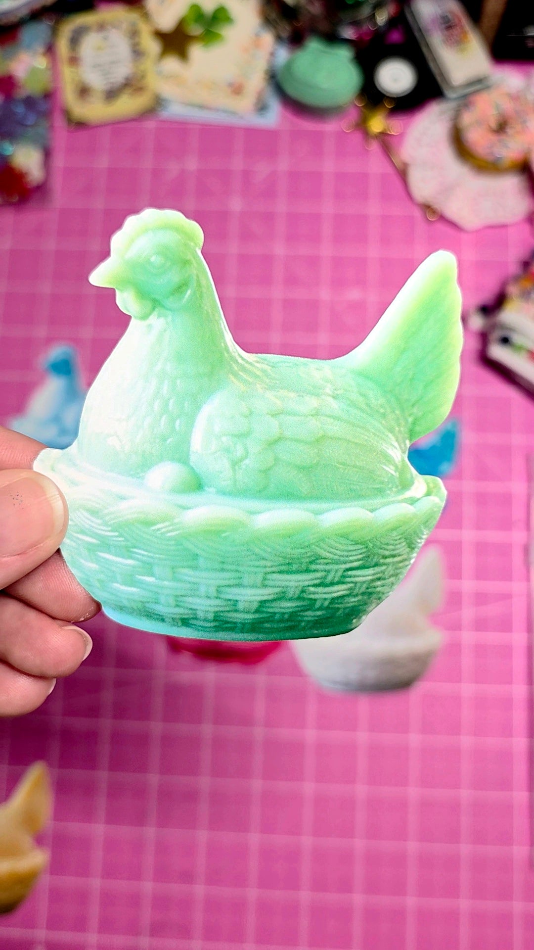 Green chicken-shaped mold held by a hand on a pink grid background