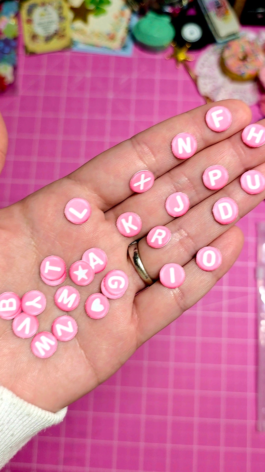 Hand holding pink letter tiles on a pink grid background