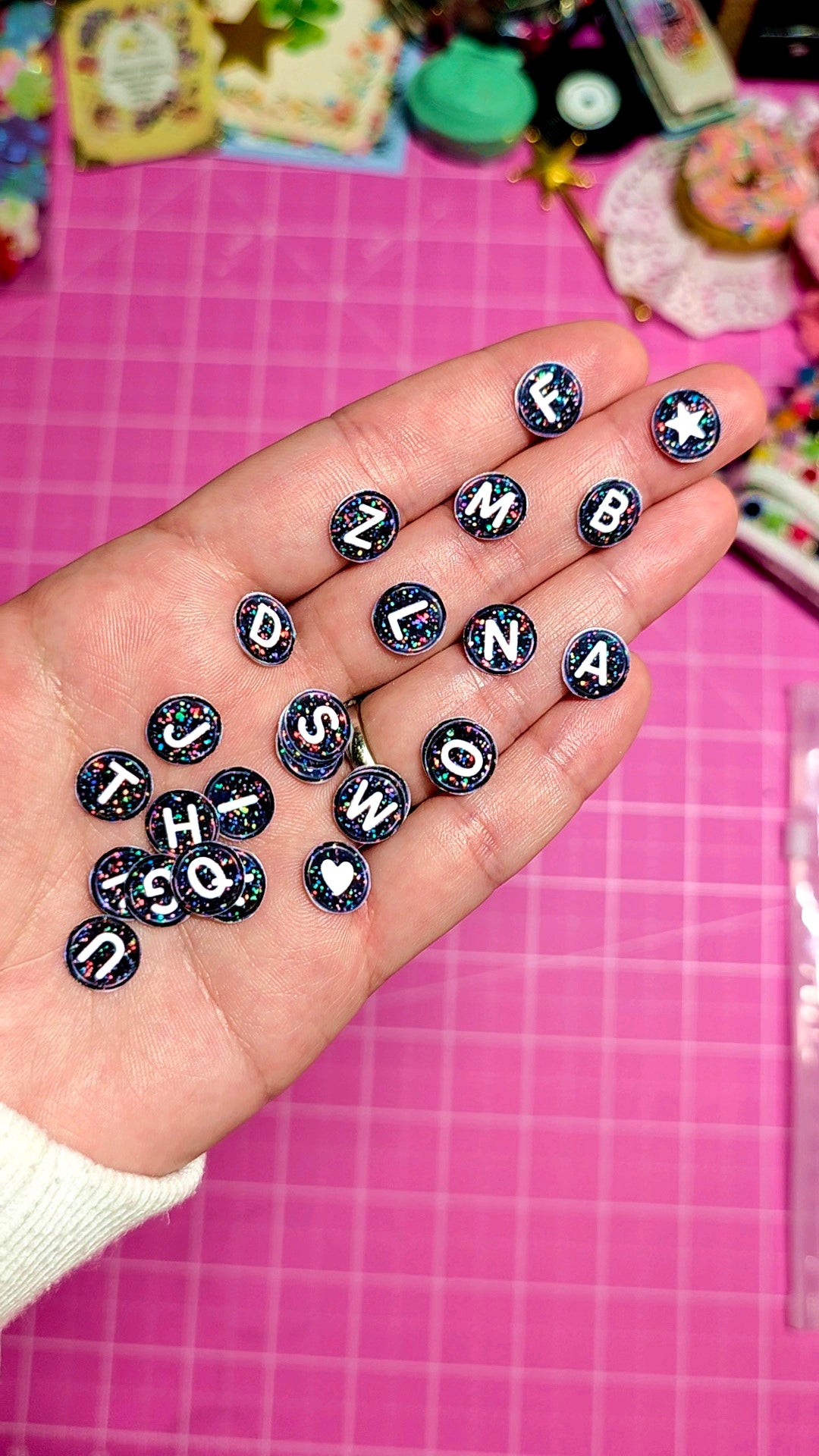 Hand holding alphabet letter charms on a pink grid background