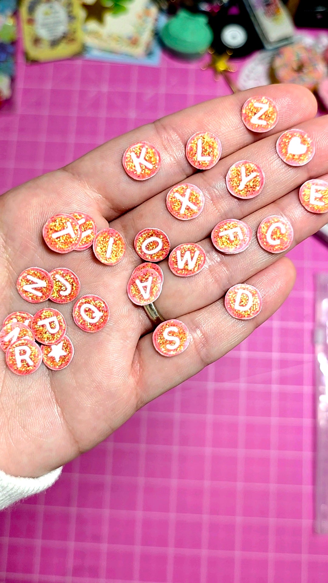 Hand holding small round decorative letters on a pink grid background