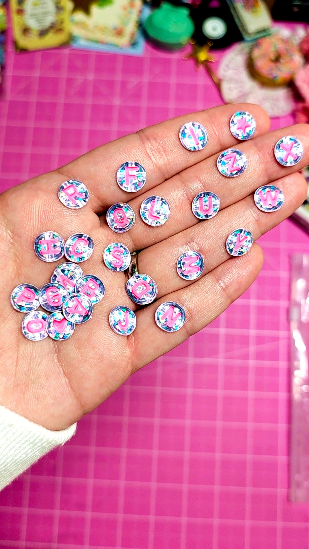 Hand holding decorative buttons with pink and blue designs on a pink grid background
