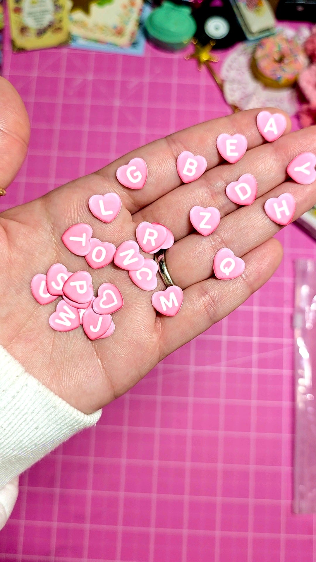 Hand holding pink heart-shaped letters on a pink grid background