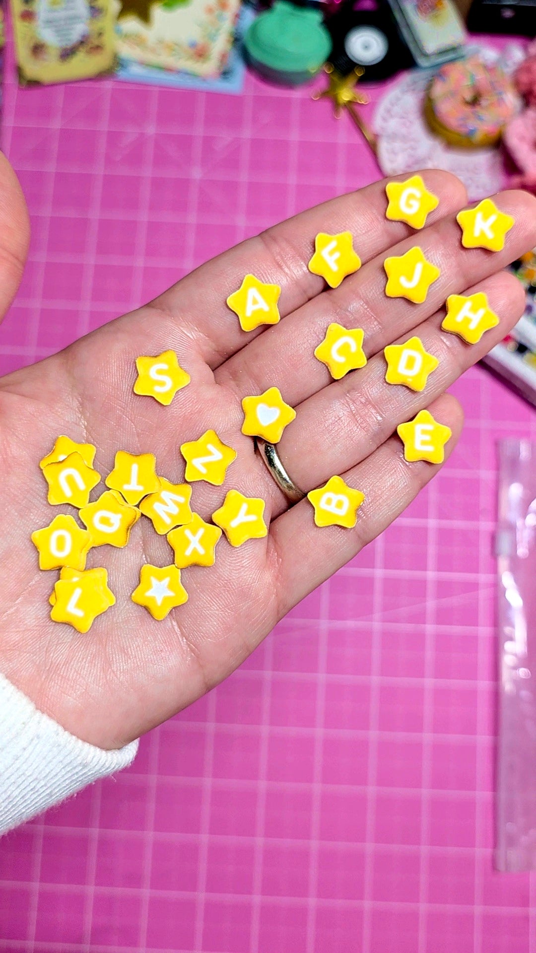 Hand holding yellow star-shaped letters on a pink grid background