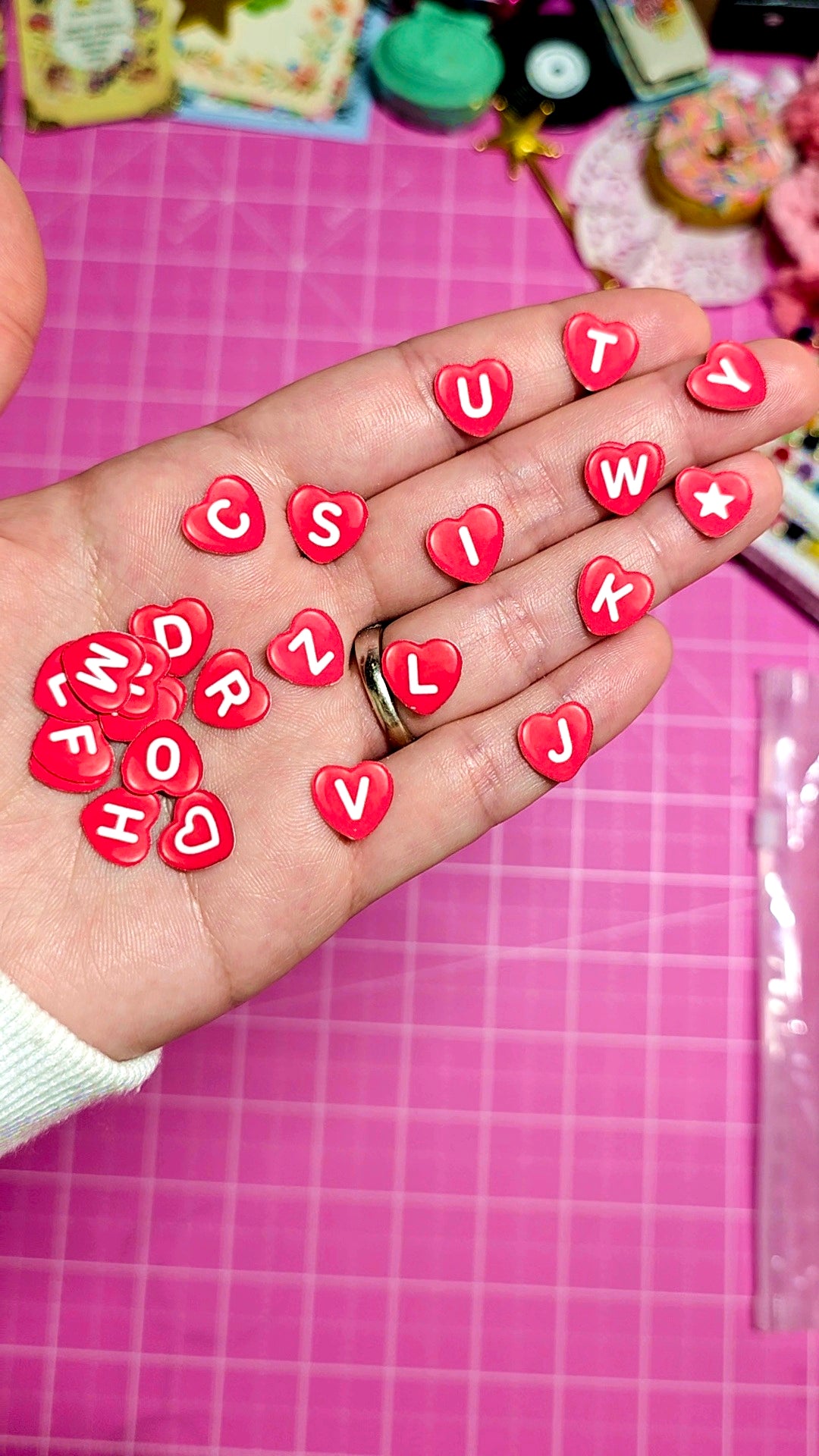 Hand holding red heart-shaped letters on a pink grid background