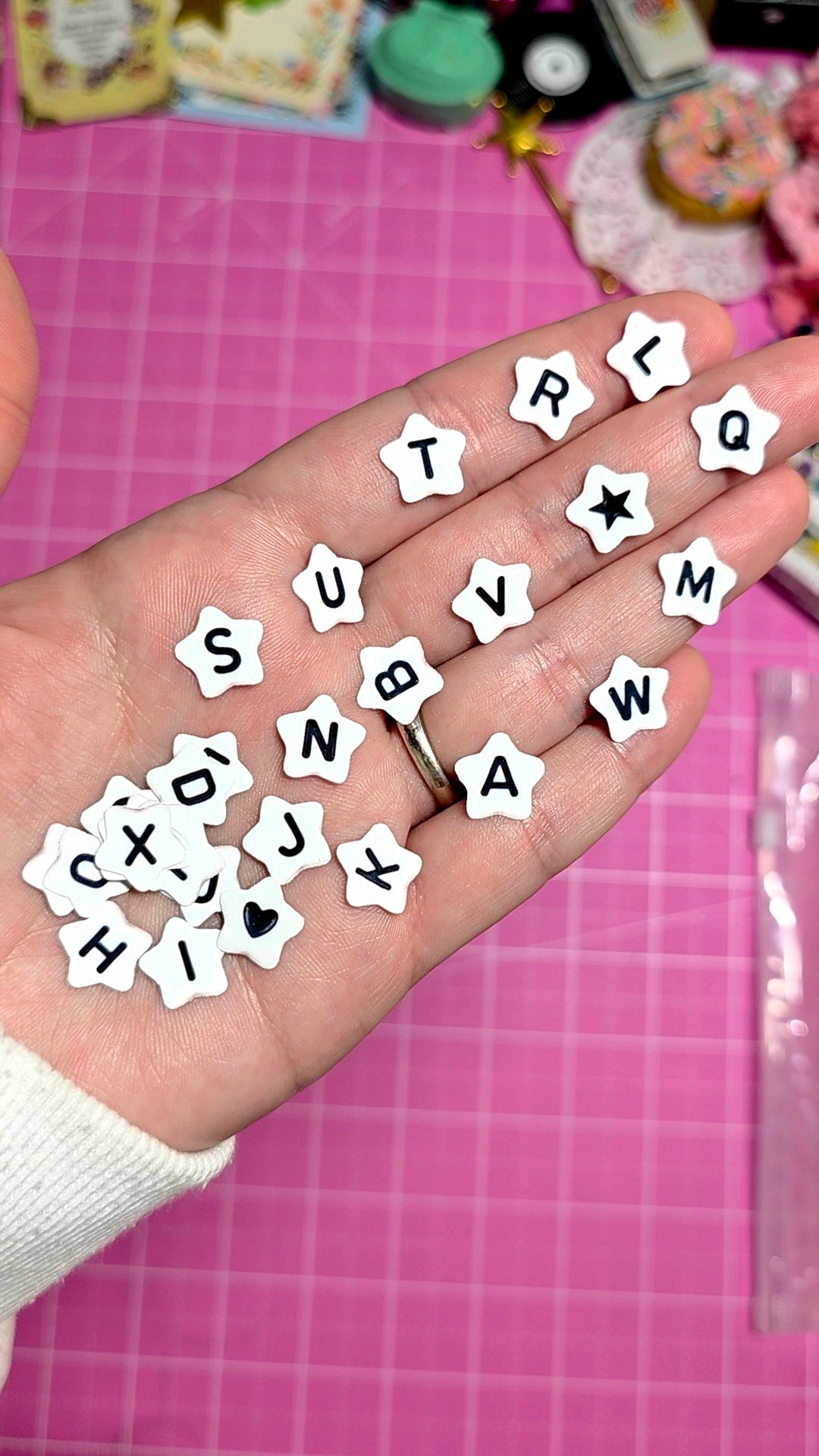 Hand holding small white letters on a pink cutting mat