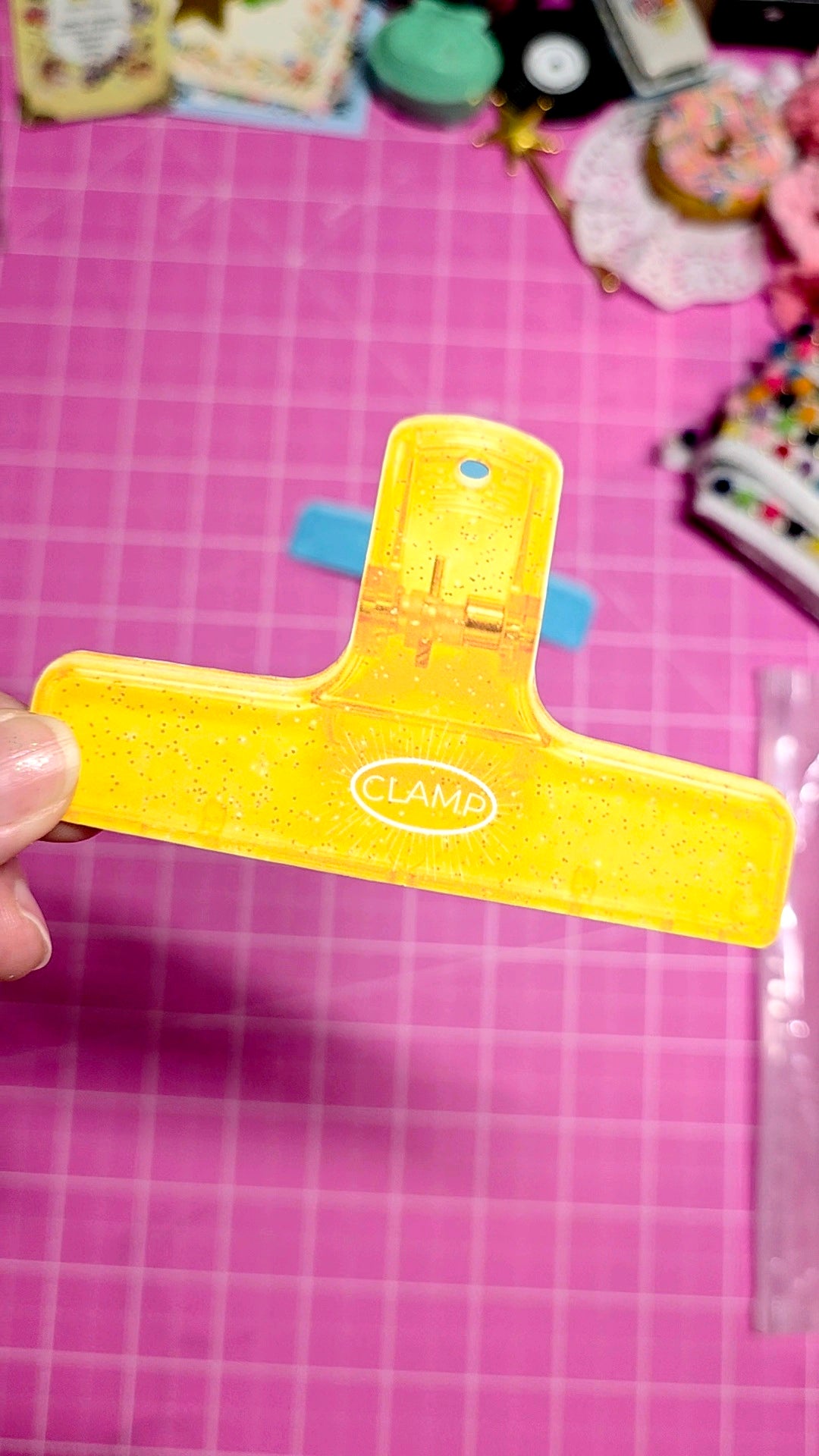 Yellow tool with 'CLAM' branding held over a pink grid background