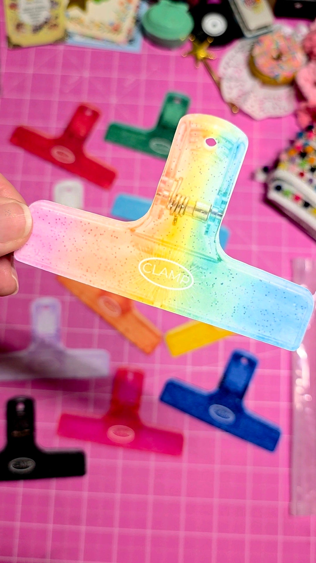 Colorful ruler with rainbow gradient held by a hand on a pink cutting mat with craft supplies.