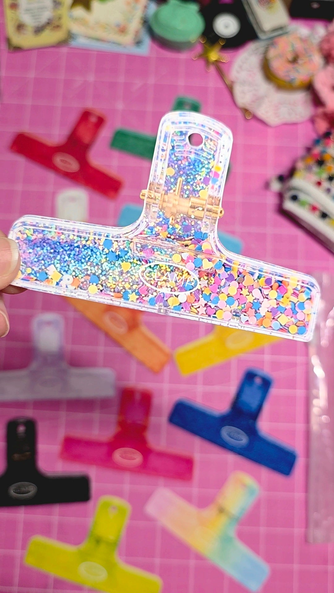 Decorative paper clip with colorful pattern on a pink cutting mat with stationery items.