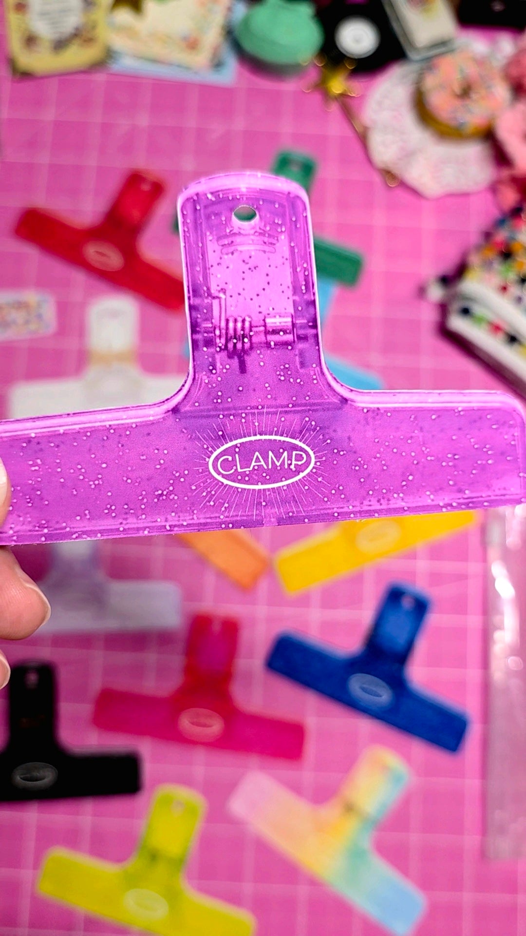 Purple CLAMP clip held over a pink cutting mat with various colored clips.