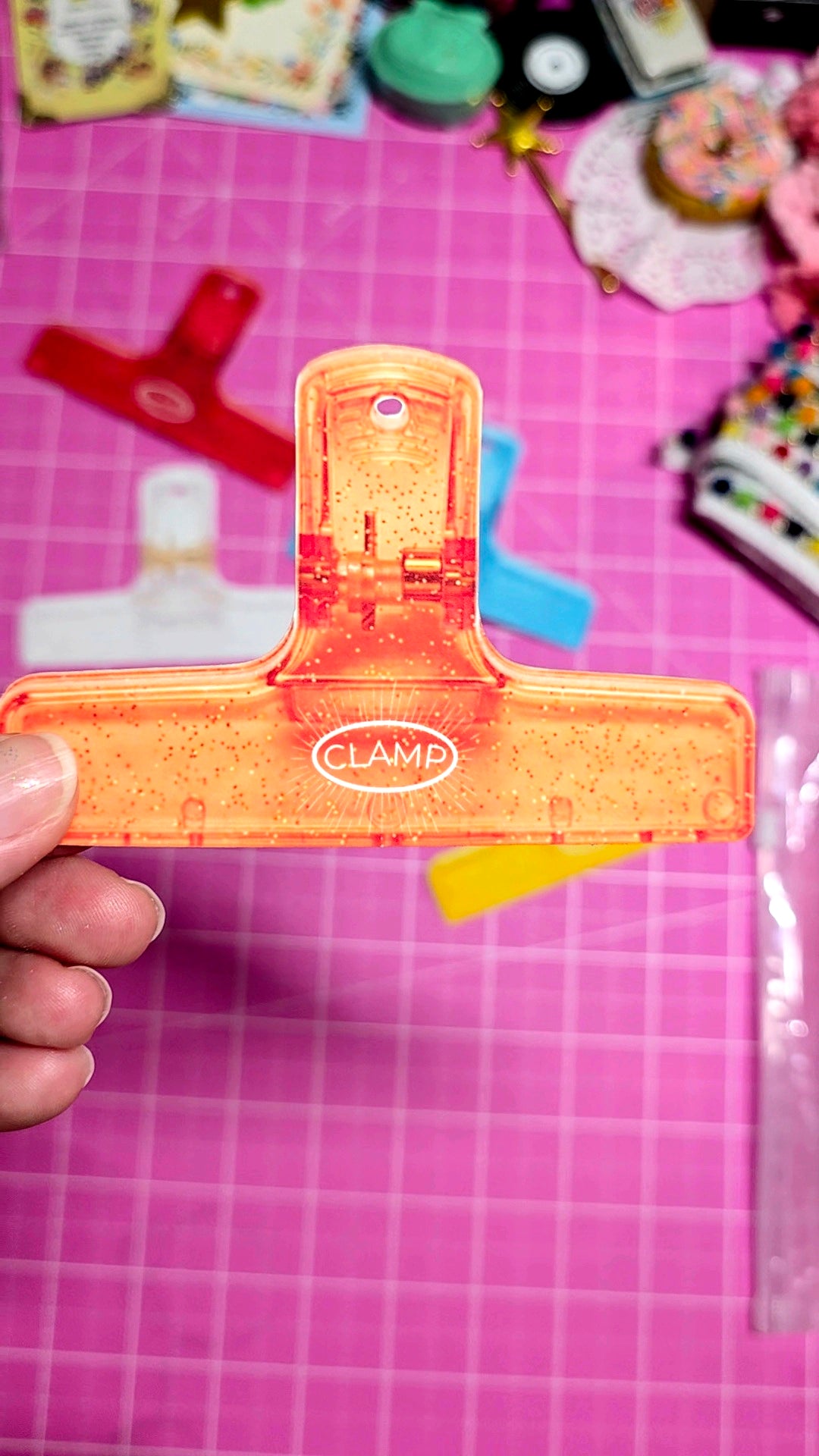Orange paper clip held by a hand on a pink grid background