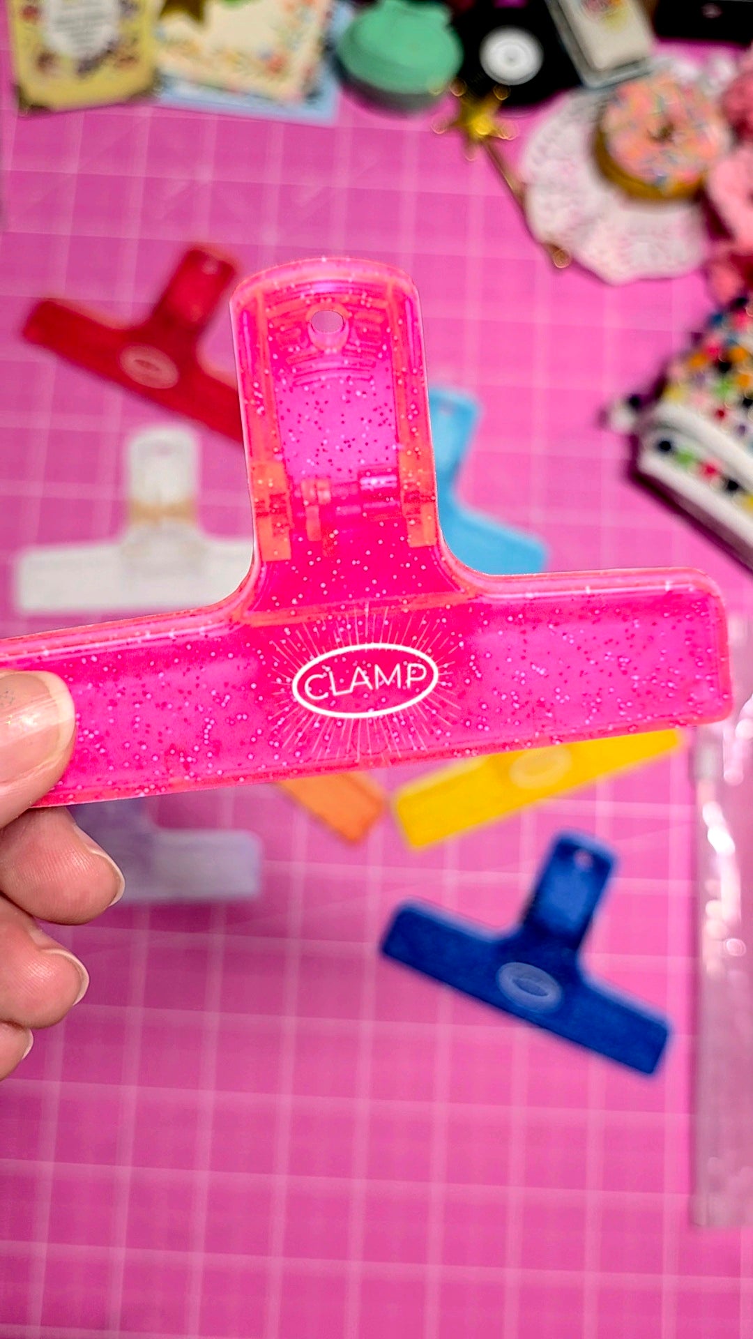 Pink paper clip held in front of a colorful background with various items.