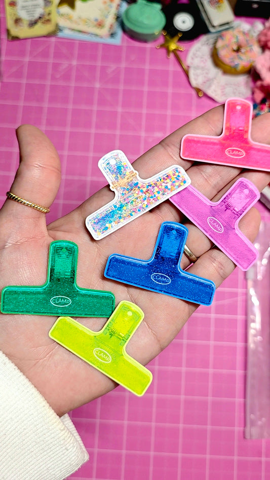 Colorful letter-shaped clips held in a hand on a pink cutting mat.