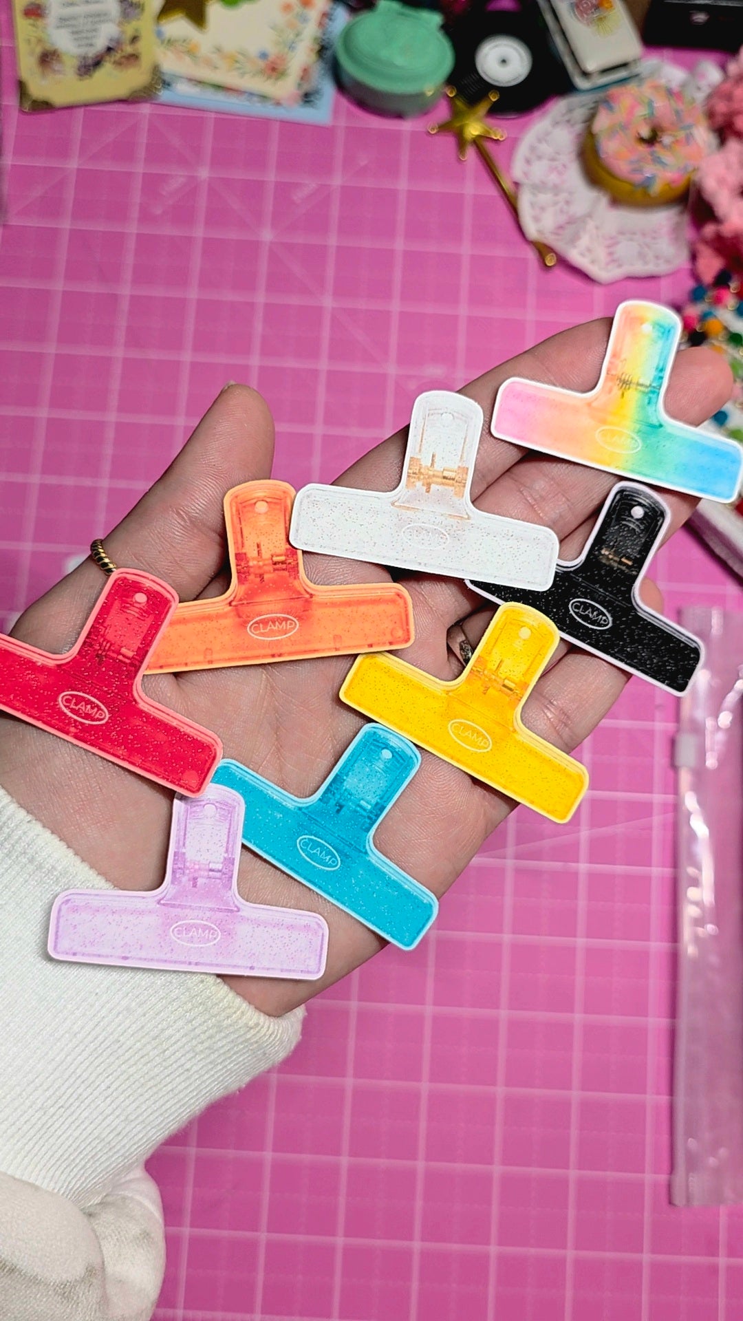 Colorful letter-shaped clips held in a hand on a pink grid background
