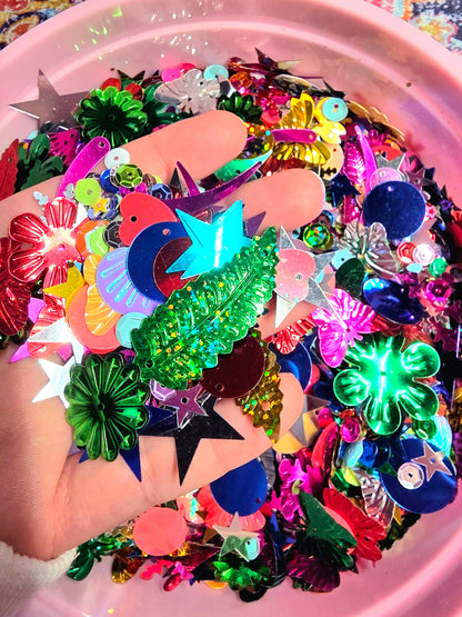 Colorful plastic embellishments held by a hand with a pink container filled with more embellishments in the background.