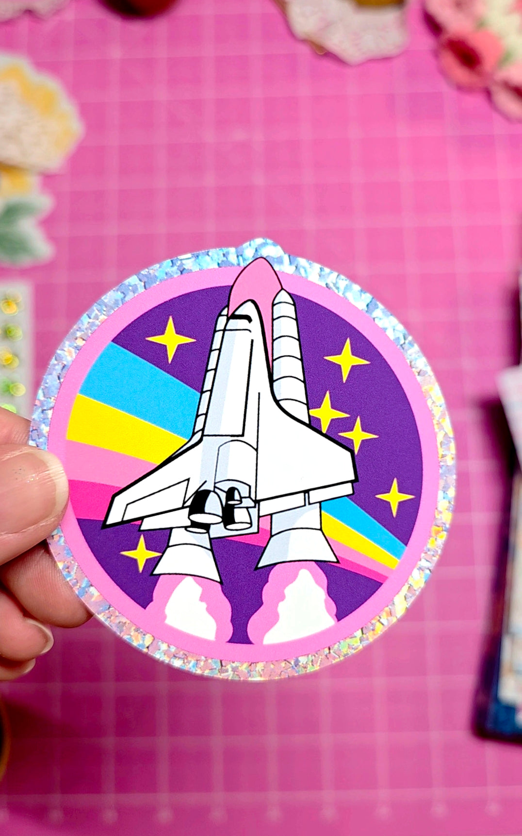 Circular sticker with a space shuttle design on a pink background