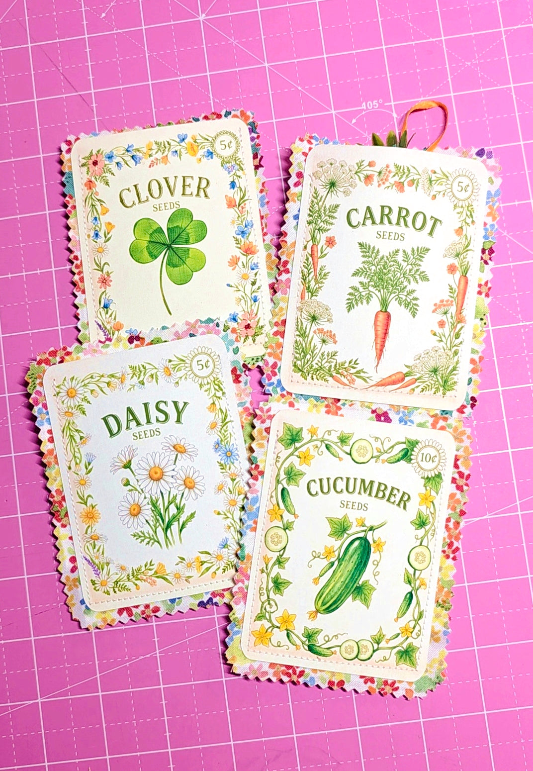 Four seed packets labeled 'Clover', 'Carrot', 'Daisy', and 'Cucumber' on a pink grid background.