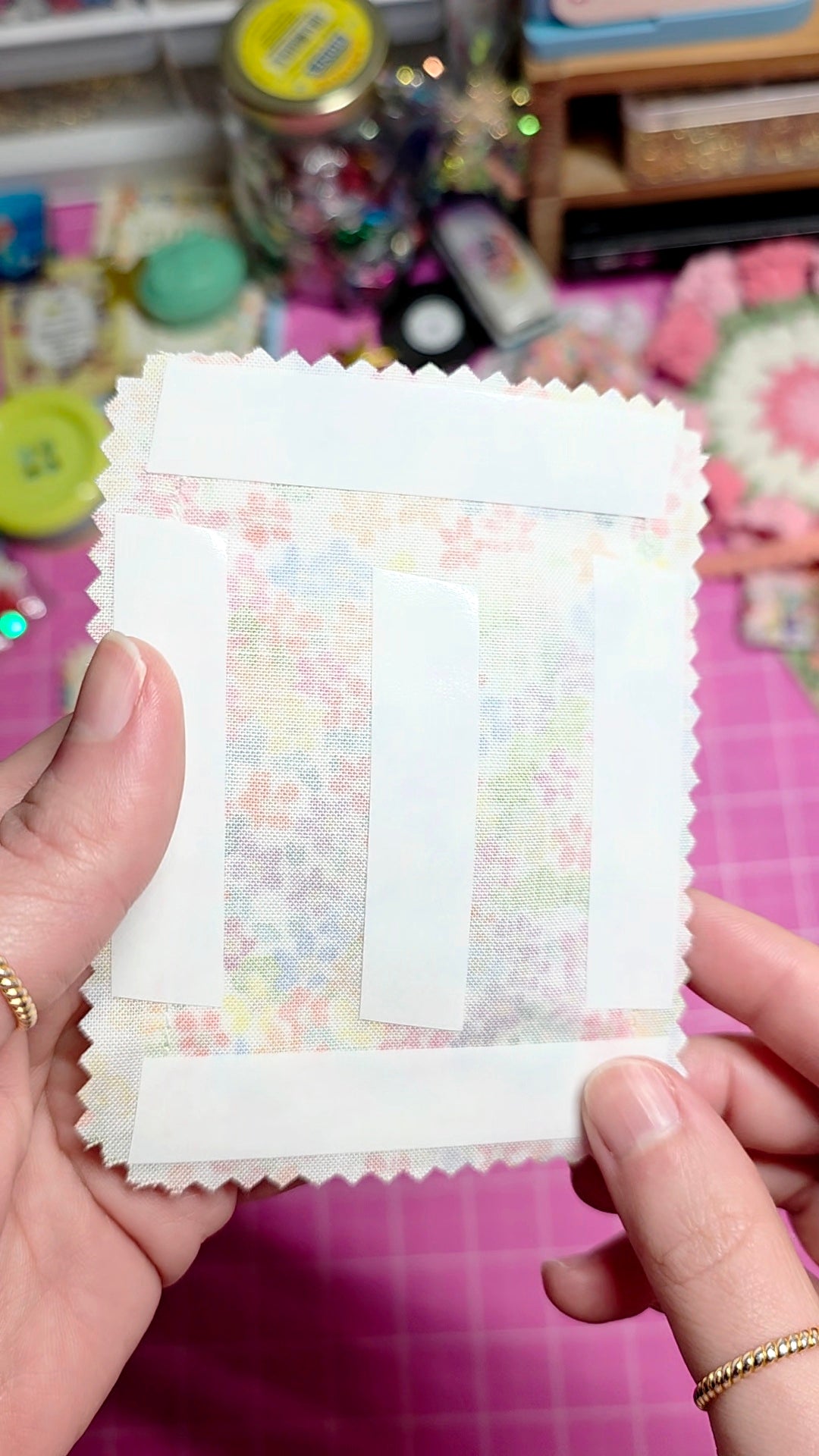 Hand holding a small package of colorful stickers on a pink surface with toys in the background