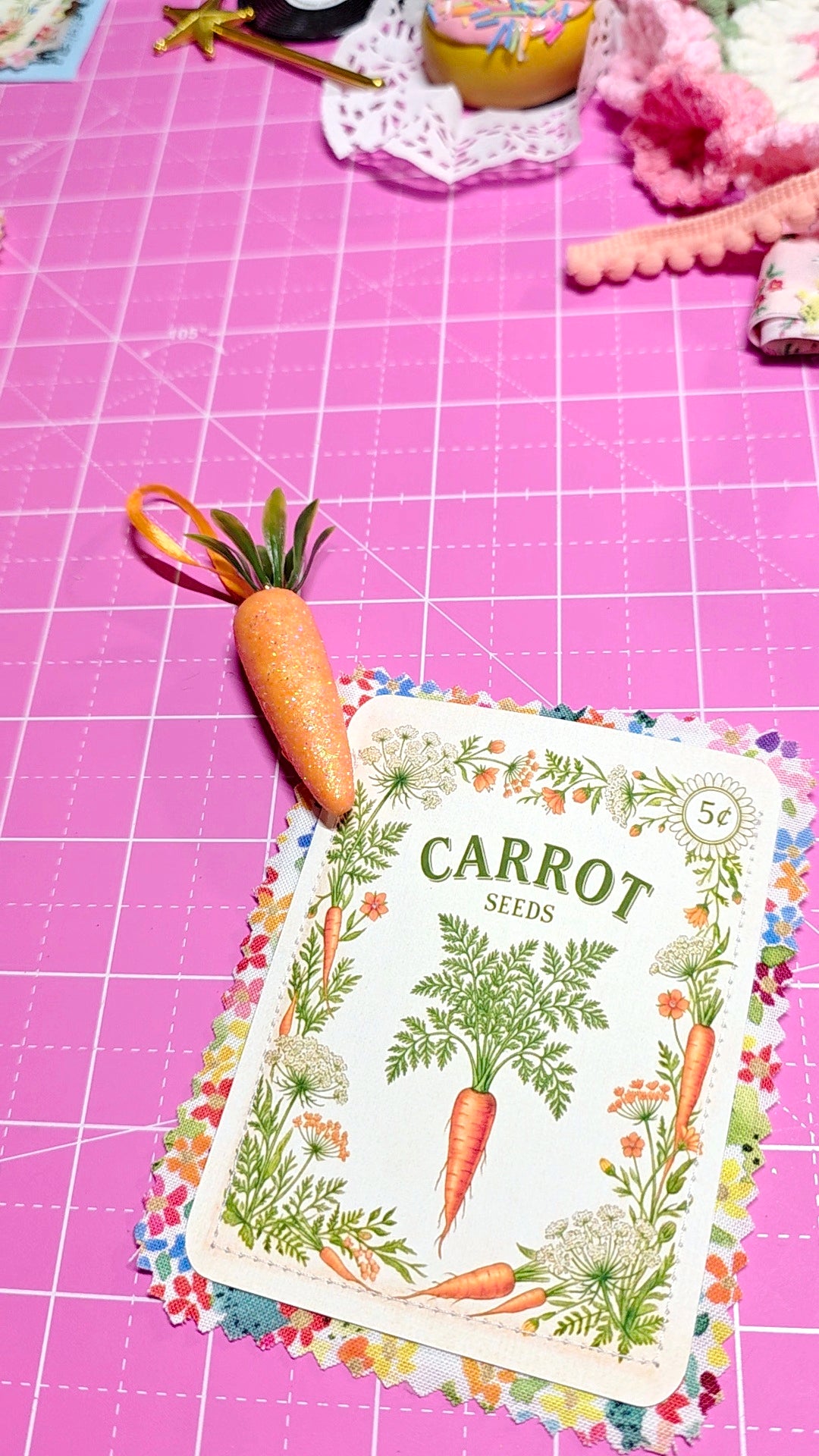 Carrot seeds packet on a pink cutting mat with a small carrot toy.