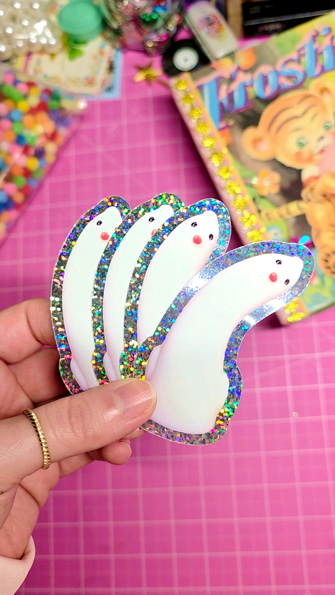 Hand holding a colorful butterfly-shaped object on a pink grid background