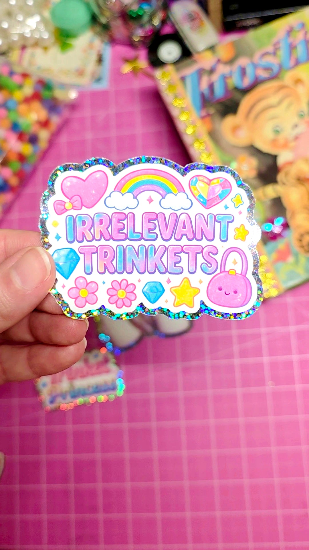 Colorful sticker with 'Irrelevant Trinkets' text held over a pink grid background