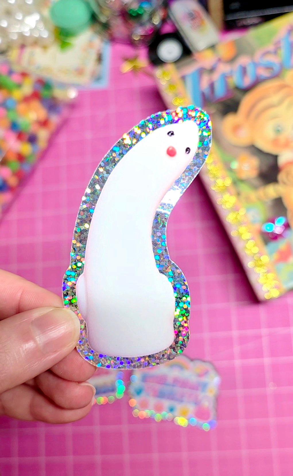 Decorative item with a white center and multicolored border held by a hand on a pink background.