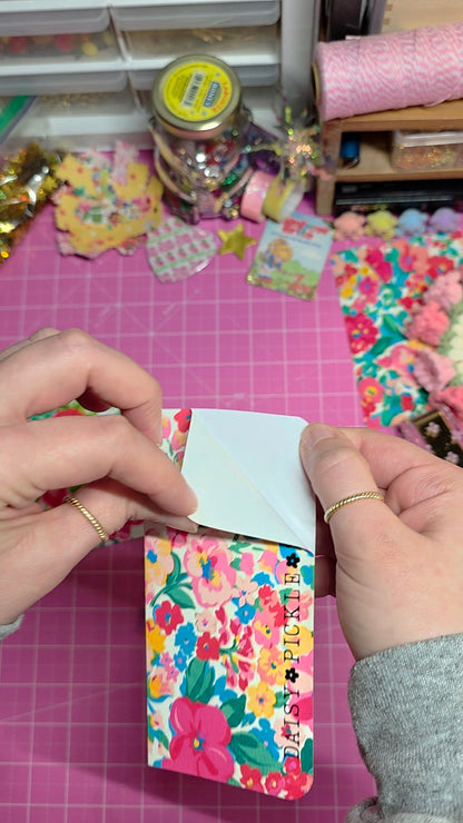 Person applying a decorative sticker to a colorful product on a craft table.