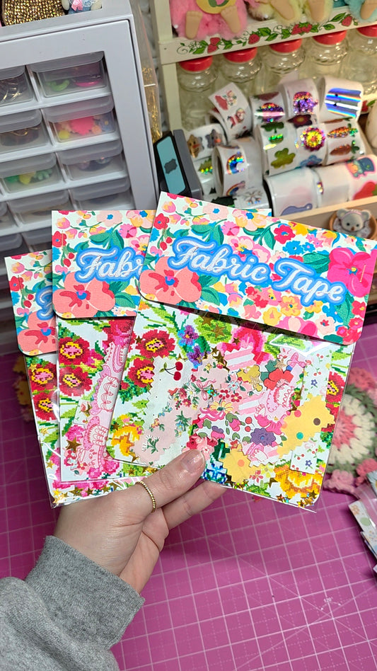 Two packages of 'Fab' fabric tape with floral designs held by a hand, with a craft store in the background.