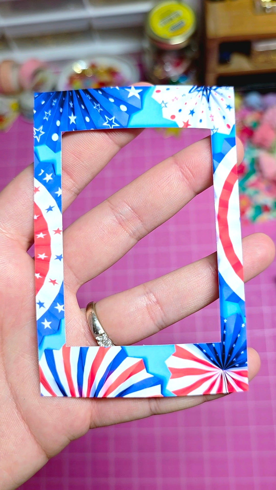Hand holding a decorative frame with red, white, and blue pattern against a blurred background